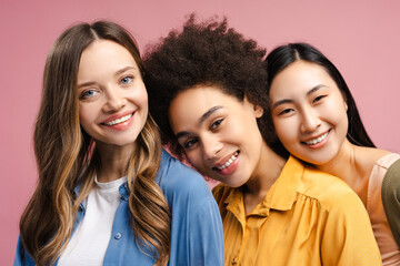 Obraz premium Three smiling young women of different ethnicities posing together on pink background
