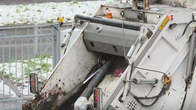 Rear loading waste collection garbage truck with bin tipper. Bin tipper mechanically lifts and inverts garbage bins in winter.