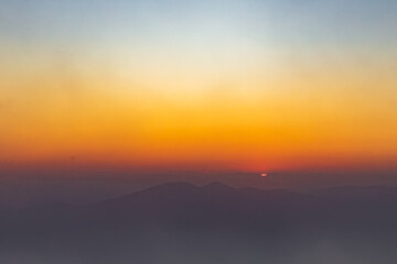 sunset in the fog, bright orange sky and silhouettes of mountain peaks