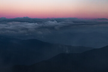 low clouds between mountain ranges against a pink sky after sunset
