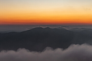 low clouds underfoot, shadows of mountain peaks in the distance against the orange sky