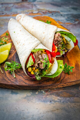 Italian style wrap piada wheat tortilla with tuna fish, vegetable and hardboiled egg served as closeup on a wooden cutting board