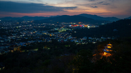 Aerial view of scenery Khao Rang viewpoint at twilight..view of a town nestled among lush green mountains at sunset, with a Pavilion structure perched on the hillside at Phuket town at Dusk