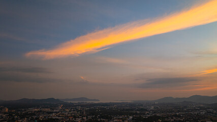 A scenic view of a town nestled among lush green mountains at sunset, with a temple structure perched on the hillside and a vibrant orange sky creating a warm, tranquil atmosphere.