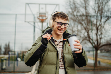 Fototapeta premium Portrait of a young smiling man student wear headphones on basketball court and hold coffee