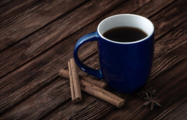 Blue cup on wooden surface. Cinnamon and star anise near a cup on the table. Natural wood texture. Hot tea or coffee in a cup.