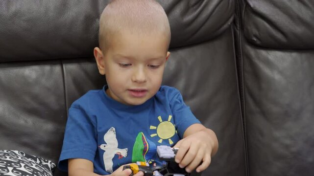 Child playing with new toy sitting on sofa at home. Concentrated face of little boy holding transformer robot toy. Three year old child examining new toy comments on his actions.