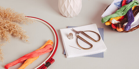 Canvas, embroidery floss, scissors, needle, thimble and cross stitch hoop on table web banner