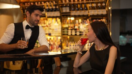 Bartender serving mixed vodka Cosmopolitan red cocktail decorated with flower making cheers with beautiful guest sitting at luxurious counter bar perfect vibrant color atmosphere nightclub. Vinosity.