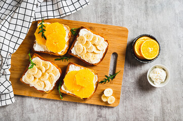 Crispy sandwiches with cottage cheese and fruits on a board on a table top view