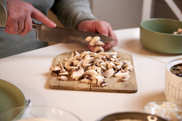 man cuts mushrooms on a wooden board on the kitchen table , close-up