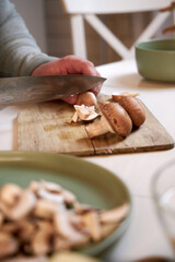man cuts mushrooms on a wooden board on the kitchen table , close-up