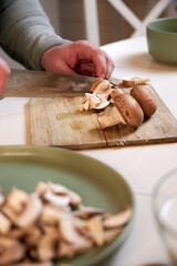 man cuts mushrooms on a wooden board on the kitchen table , close-up