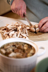 man cuts mushrooms on a wooden board on the kitchen table , close-up