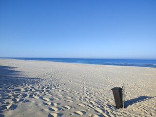 black trash can stands on a deserted beach on a sunny day