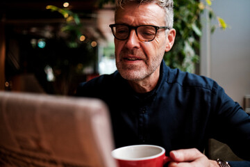 Senior businessman reading newspaper and drinking coffee in cafe