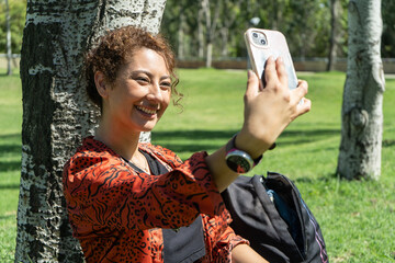 Smiling student taking selfie under tree in park