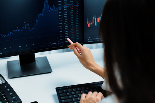 Young beautiful Asian businesswoman pointing with pen in exchange stock market on pc screen at back side view, analyzing profit at modern office, investing high profit valed in wealth. Stratagem.