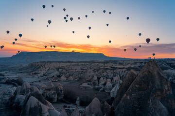 Aerial view of numerous hot air balloons floating above rock formations in Cappadocia, Turkey, in the morning light
