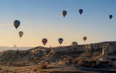 Many hot air balloons flying over rock formations in Cappadodia , Turkey