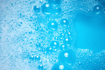 Small and big bubbles in blue water. Abstract white soap foam texture. Concept of cleaning and washing.
