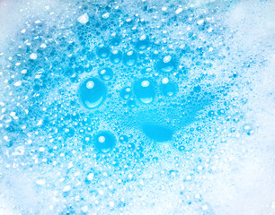 Small and big bubbles in blue water. Abstract white soap foam or soap suds texture. Concept of cleaning and washing.