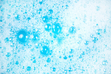 Small and big bubbles in blue water. Abstract white soap foam or soap suds texture. Concept of cleaning and washing.