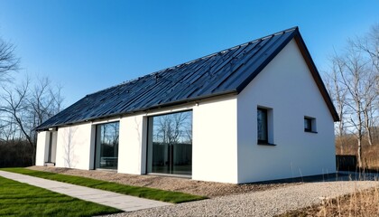 Obraz premium a modern white house with a black metal roof and large windows set against a blue sky.