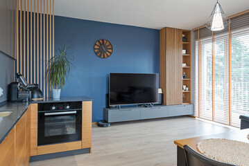 Modern living room in stylish interior with blue wall with tv and clock and window with blinds. Minimalism and luxury in room and new home.