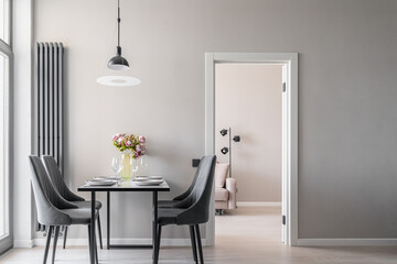 design of modern apartment in calm shades of gray and beige. Kitchen interior. plates, glasses, and vase of pink flowers on kitchen table. table and grey chairs in kitchen. Modern flat. inside home
