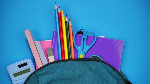 From the school bag appear notebooks, pencils and pens and other school supplies. Back to school concept. Stop motion