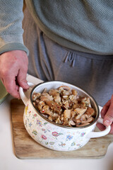 fried mushrooms with onions lying in an enameled white pot, close-up view from above