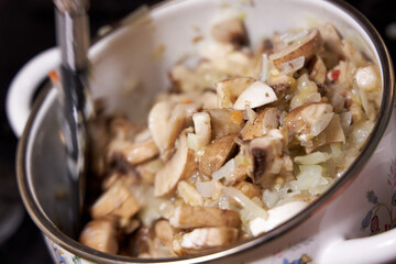 fried mushrooms with onions lying in an enameled white pot, close-up view from above