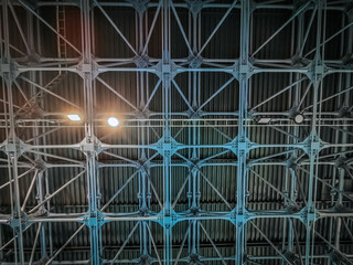 A detailed view of an industrial metal ceiling with an intricate grid structure. The blue lighting...