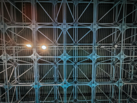 A detailed view of an industrial metal ceiling with an intricate grid structure. The blue lighting highlights the strong framework, showcasing engineering and architectural design in a modern facility