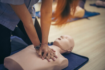 Close-up of Asian hands practicing cardiopulmonary resuscitation (CPR) on a training dummy. Important techniques include chest compressions and maintaining an airway.