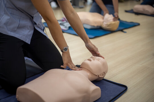 Close-up of Asian hands practicing cardiopulmonary resuscitation (CPR) on a training dummy. Important techniques include chest compressions and maintaining an airway.