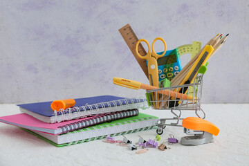 Tiny shopping cart with stationery on table against grey background