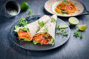 Italian style wrap piada tortilla with cured graved salmon, salad and zucchini served as close-up with avocado sour cream dressing dip on a Nordic Design plate