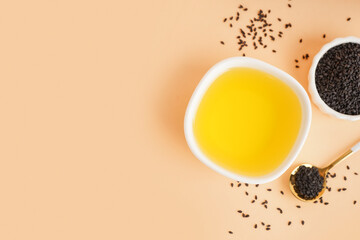 Bowls of oil and sesame seeds with spoon on orange background