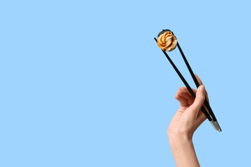 Hand with tasty sushi roll and chopsticks on blue background © Pixel-Shot