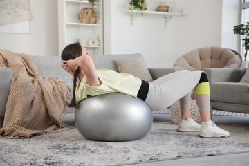 Sporty young woman doing exercises on fitness ball at home