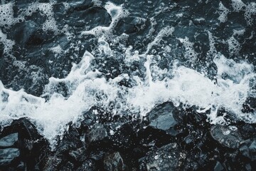 Obraz premium Waves crash against rocky shore as sea foam forms under a cloudy sky near the coastline
