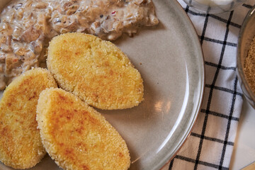 potato cutlets with mushrooms in sour cream on a beige ceramic plate, top view