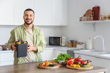 Young man with compost bin and vegetable scraps during cooking in kitchen