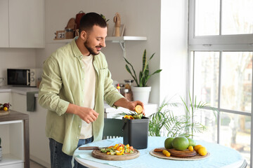 Young man with compost bin and vegetable scraps during cooking in kitchen
