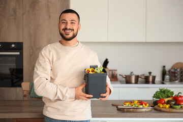 Young man with vegetable scraps in compost bin in kitchen