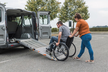 Naklejka premium Female assistant pushing a man with disability, a wheelchair user up the car ramp into the van. Accessibility and travel concepts.
