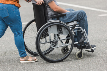 Obraz premium Personal assistant helping a man with disability to push a wheelchair outdoors. Help service concept.