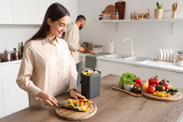 Young woman with compost bin and vegetable scraps during cooking in kitchen